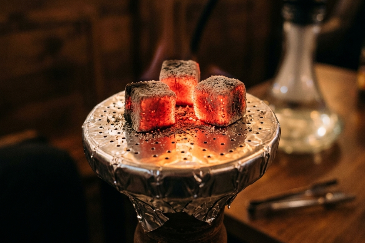 Nahaufnahme: Glühende Kohle auf Alufolie über einem Shisha-Kopf – gleichmässig rote Glut sichtbar